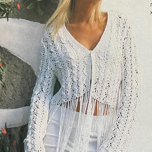 Può includere: Un cardigan bianco a trama aperta con maniche lunghe e scollo a V. Il cardigan presenta un dettaglio a frange sull'orlo. Il capo è realizzato in un tessuto delicato a maglia aperta, creando un aspetto strutturato. Lo stile è bohémien.