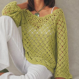 May include: A lime green long-sleeved crochet sweater featuring an intricate openwork pattern, a wide neckline, and a loose fit. The garment is worn over a white camisole and paired with white trousers, showcasing a detailed knit texture throughout.