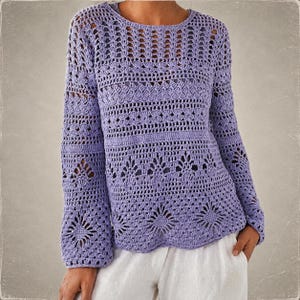 May include: A long-sleeved lavender crochet sweater featuring a complex openwork pattern with repeating geometric and floral motifs. The garment has a round neckline and a semi-sheer texture, showcasing intricate needlework throughout the body and sleeves.