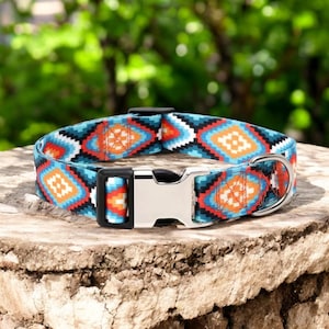 Puede incluir: Un collar de perro colorido con un patrón geométrico en tonos de azul, naranja y blanco. El collar tiene una hebilla plateada y un anillo en D.