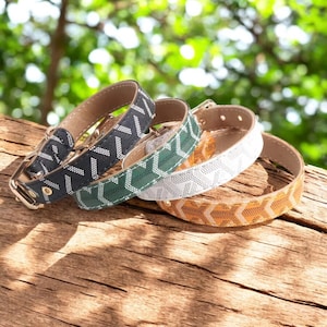 May include: Four dog collars in different colours and patterns. The collars are made of leather and have a geometric design. The collars are stacked on top of each other.