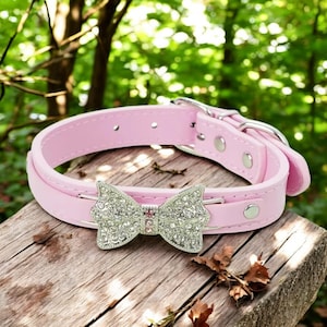 Pode incluir: Coleira de cachorro de couro rosa com um laço prateado adornado com strass.