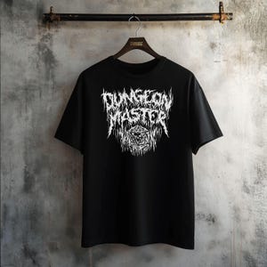 May include: Black t-shirt featuring a white graphic print of "DUNGEON MASTER" in a metal font with a stylized die in the centre.