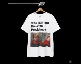 May include: White t-shirt with a black and white image of a man in a mugshot. The text "WANTED FOR the 47th Presidency" is printed on the shirt.