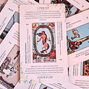 May include: The World tarot card with a pink background and white text. The card depicts a woman standing inside a wreath with a lion and an eagle. The text on the card reads "The World". The card's keywords are listed below the image. The keywords for the upright card are: Completion, Fulfillment, Wholeness, Success. The keywords for the reversed card are: Stagnation, Delayed success, Lack of closure, Incompletion, Resistance, Frustration.