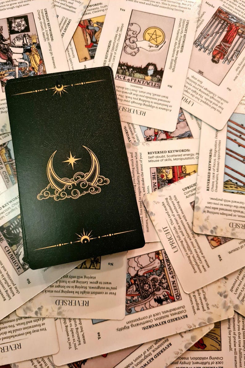 May include: A close-up of a green tarot card with a gold crescent moon and star design. The card is surrounded by other tarot cards with white backgrounds and black text.
