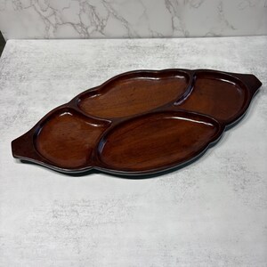 May include: A dark brown, wooden serving tray with four compartments. The tray has a unique, organic shape with rounded edges and a glossy finish. The tray is designed for serving snacks or appetizers.
