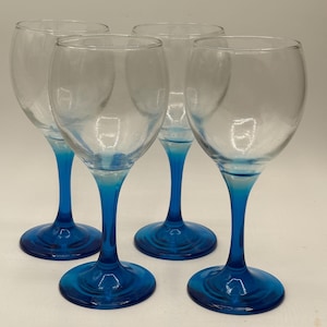 May include: Four clear wine glasses with vibrant blue stems and bases. The glasses have a classic rounded bowl shape, perfect for serving wine. The blue color adds a pop of color to the glassware.