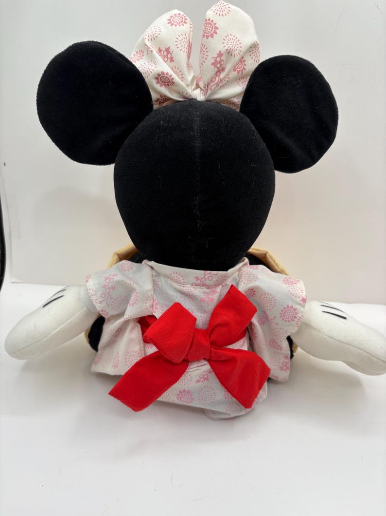May include: A plush toy featuring a black head with large round ears and white gloves. The toy wears a white and pink floral patterned kimono with a large red bow. A matching bow adorns the head.