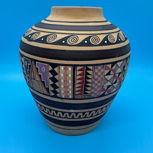 May include: A handcrafted ceramic vase with a beige base and a dark brown top. The vase features intricate geometric patterns in black, purple, red, and white. The design includes spiral and wave motifs, creating a unique decorative piece.