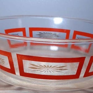Peut inclure: Un bol mélangeur en verre transparent orné d'un motif répétitif de bordures rectangulaires orange. À l'intérieur de chaque rectangle orange se trouve un motif en forme d'étoile ou de fleur blanche. Le bol présente un large bord circulaire.