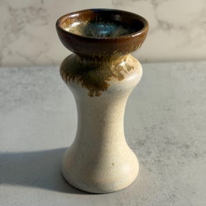 Peut inclure: Petit récipient en céramique fait à la main, avec une base arrondie et un dessus évasé. Le dessus est brun foncé, passant à un bronzage plus clair avec des accents verts et bleus. Le corps est de couleur blanc cassé moucheté.