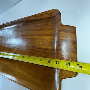 May include: A wooden serving tray with a rectangular shape and rounded edges. The tray is a warm brown colour and appears to be made of a hardwood. The tray measures approximately 61 cm long.