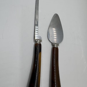 May include: A vintage cake knife and server set. The knife has a serrated blade and a brown and amber handle. The server has a rounded blade and a matching brown handle. Both pieces have silver-toned metal accents.