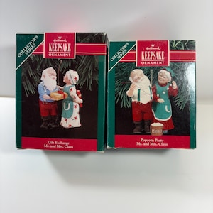 May include: Two Hallmark Keepsake Christmas ornaments in their original boxes. One box features a Mr. and Mrs. Claus ornament titled "Gift Exchange." The other box features a Mr. and Mrs. Claus ornament titled "Popcorn Party" from 1990.