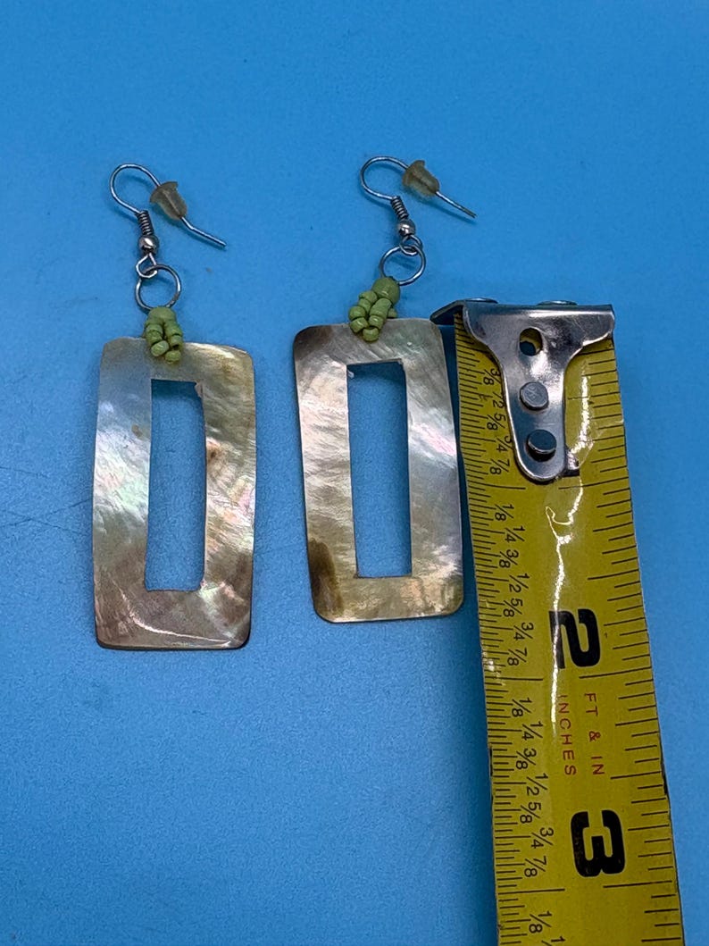 K&ouml;nnte beinhalten: Rechteckige H&auml;ngeohrringe mit Perlmutt-Finish. Die Ohrringe sind ca. 6,35 cm lang. Jeder Ohrring hat einen silberfarbenen Haken und eine kleine Gruppe gr&uuml;ner Perlen oben.
