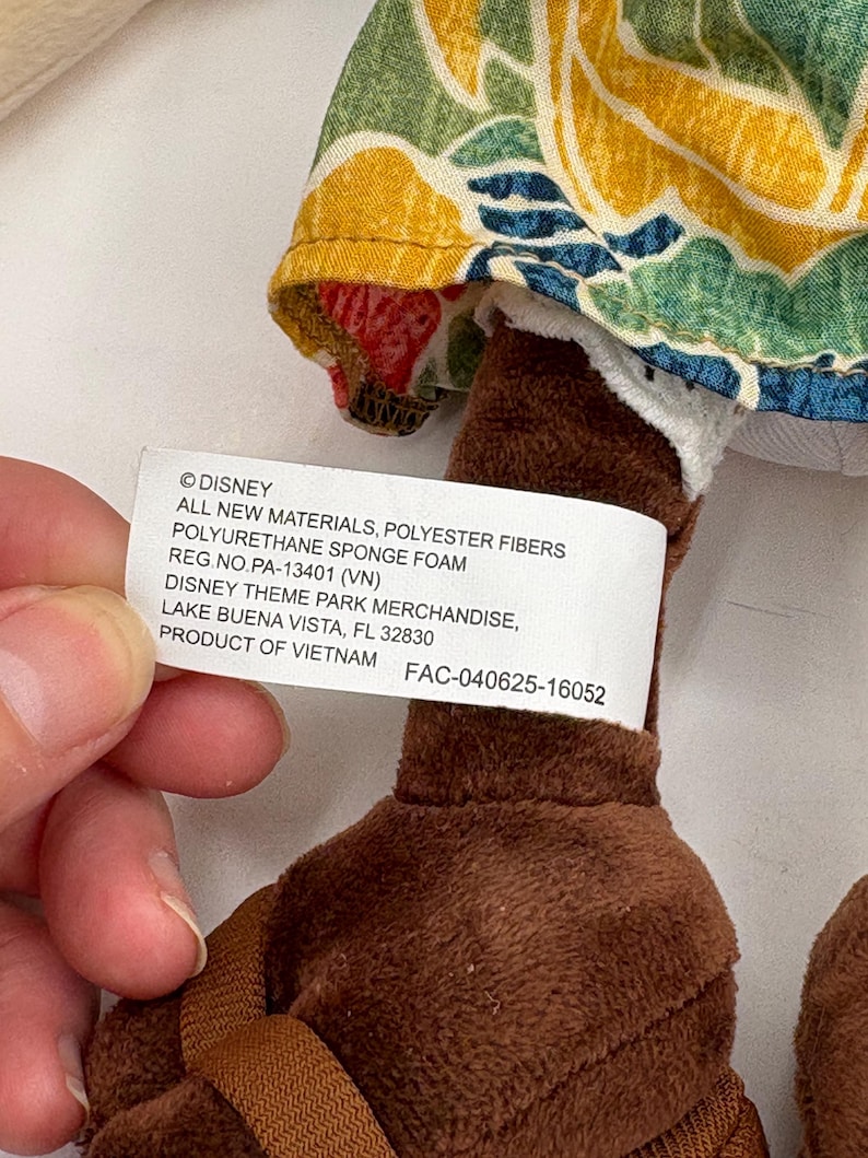 May include: A plush toy with brown legs and a floral patterned fabric. The tag reads "&copy;DISNEY" and "DISNEY THEME PARK MERCHANDISE, LAKE BUENA VISTA, FL 32830". The toy is made of polyester fibers and polyurethane sponge foam.
