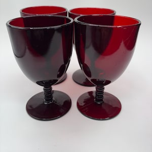 May include: Four ruby red wine glasses with a rounded bowl and a black, ribbed stem. The glasses have a dark, glossy finish and are arranged on a white surface. The glasses are a vintage style.