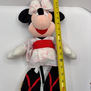 May include: A Minnie Mouse plush toy, approximately 16 inches tall, wearing a pink and white floral kimono with a red obi. The toy has black ears, a pink face, and a red bow.