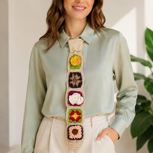 Peut inclure: Une cravate en crochet beige ornée de cinq motifs carrés aux dessins floraux et géométriques en jaune, marron foncé, blanc, rouge et rose, portée avec une chemise boutonnée en satin vert clair et un pantalon crème.