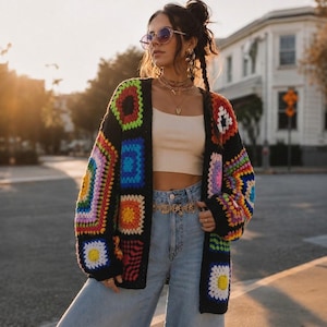 Peut inclure: Un gilet à manches longues composé de carrés granny bordés de noir dans des couleurs vives, notamment rouge, orange, jaune, vert, bleu et violet. Le vêtement est porté sur un débardeur court beige et un jean bleu clair avec une ceinture dorée.
