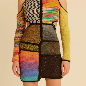 Peut inclure: Une robe en crochet patchwork avec un col montant et des côtés découpés. La robe présente une variété de couleurs, dont le jaune, l'orange, le noir et le bleu. Les manches longues sont détachées. Un collier ras du cou noir complète le look.