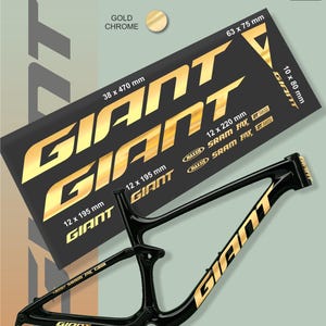 Puede incluir: Cuadro de bicicleta negro con letras doradas "GIANT" y una hoja de pegatinas cromadas doradas. La hoja de pegatinas tiene varios tamaños, incluyendo 38 x 470 mm y 63 x 75 mm. El cuadro también tiene la marca "GIANT".
