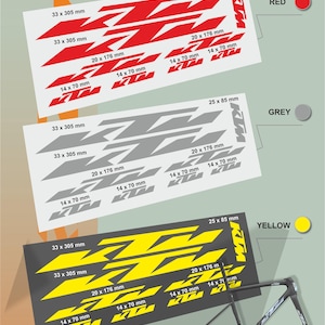 May include: Three sets of KTM motorcycle decals in red, gray, and yellow. Each set includes various sizes, such as 33 x 305 mm, 20 x 176 mm, and 14 x 70 mm. A black motorcycle frame is also visible.