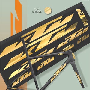 May include: A black bicycle frame with gold chrome accents and the KTM logo. The frame is positioned in front of a black background with gold KTM logos. The words "Gold Chrome" are visible.