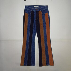 May include: High-waisted trousers featuring a vertical striped pattern in alternating panels of blue denim, black corduroy, and brown corduroy. The garment has a button and zip fly closure, belt loops, and a slightly flared leg silhouette.