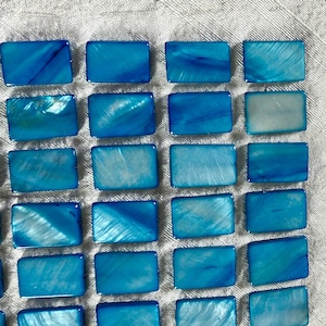 May include: A collection of rectangular, iridescent blue tiles arranged in a grid pattern. The tiles have a glossy finish and varying shades of blue, creating a shimmering effect. The tiles are likely for decorative purposes.