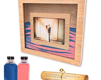 Könnte beinhalten: Ein hölzerner Hochzeitsfotorahmen mit einem Bild eines Paares, blauem und rosa Sand und zwei Sandflaschen. Eine Schriftrolle mit Text ist ebenfalls enthalten. Der Rahmen hat eine helle Holzoberfläche.
