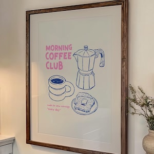 Op de afbeelding: Een keukeninterieur met een ingelijste print met de tekst "Morning Coffee Club" en illustraties van koffie-gerelateerde items. Een fornuis, kasten en een houten tafel met borden en kaarsen zijn ook zichtbaar.