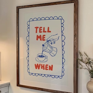 Könnte beinhalten: Küchenszene mit einem gerahmten Druck mit der Aufschrift "TELL ME WHEN". Die Küche hat einen Edelstahlherd, eine Dunstabzugshaube und einen Holztisch mit Tellern und einer Tasse. Zwei große Kerzen sind angezündet.