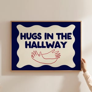 Puede incluir: Una impresión enmarcada con un fondo azul y un borde blanco en forma de nube. El texto "HUGS IN THE HALLWAY" está escrito en letras negras y negritas. Dentro de la nube, se dibujan dos brazos rojos, abrazándose.