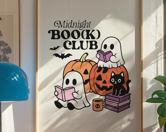 May include: A framed print with the text "Midnight BOO(K) CLUB" featuring cartoon ghosts, pumpkins, and a black cat. The ghosts are reading books, and the pumpkins are orange. A coffee mug is also present.