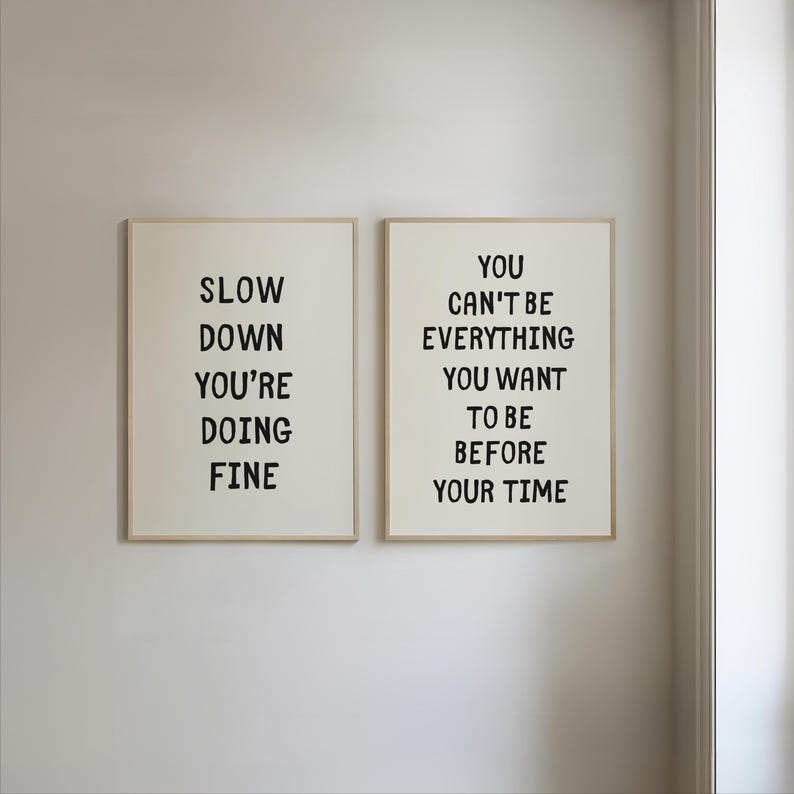 May include: Two framed art prints with inspirational quotes. The left print reads "SLOW DOWN YOU'RE DOING FINE" in black text. The right print says "YOU CAN'T BE EVERYTHING YOU WANT TO BE BEFORE YOUR TIME".