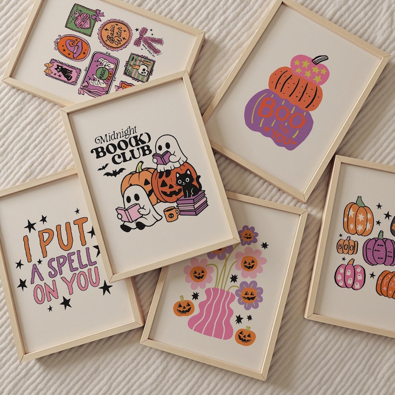 May include: A collection of framed Halloween-themed art prints. The prints feature illustrations of pumpkins, ghosts, and floral arrangements in a retro style. One print reads "I PUT A SPELL ON YOU," and another says "Midnight Book Club."