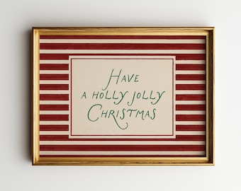 May include: A framed print with a gold-coloured frame. The print has a red and white striped background with a cream-coloured rectangle in the centre. The text "Have a holly jolly Christmas" is written in green cursive.