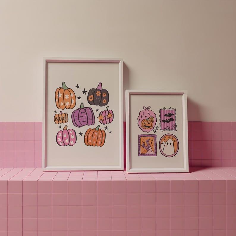 May include: Two framed Halloween-themed art prints. The larger print features illustrated pumpkins in orange, pink, and purple with star accents. The smaller print showcases a pumpkin, bats, and a ghost. Both prints are in white frames.