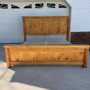 May include: A wooden bed frame featuring a tall headboard and a matching footboard, both constructed from light brown stained wood with visible grain and knots. The frame includes a series of horizontal wooden slats for mattress support.