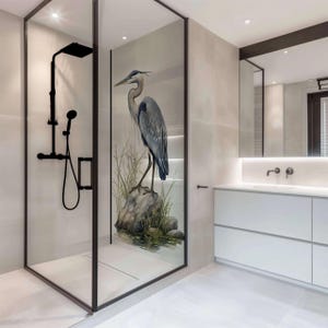 Può includere: Un bagno moderno con una cabina doccia in vetro che presenta una grande illustrazione dettagliata di una garzetta grigia in piedi su uno scoglio in uno stagno. La doccia ha un soffione nero e un pavimento in piastrelle bianche.