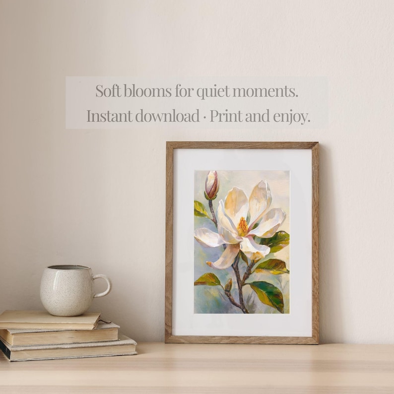 May include: A framed floral print featuring a white magnolia blossom with yellow center and green leaves. The artwork is in a wooden frame and rests on a wooden surface. Text above the frame reads: "Soft blooms for quiet moments. Instant download - Print and enjoy."