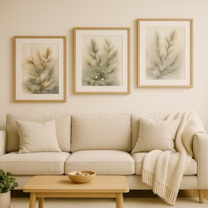 Puede incluir: Tres láminas artísticas botánicas enmarcadas con marcos de madera marrón claro. La obra presenta ilustraciones al estilo acuarela de ramitas de plantas en tonos verdes, beige y marrón. Las láminas cuelgan sobre un sofá beige con cojines a juego.
