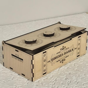 Puede incluir: Una caja de madera de color claro con tapa con bisagras y tres diales circulares en la parte superior. La caja está etiquetada como "GIMENES BANKA" y "FOR INVESTMENT". El diseño sugiere un banco o una caja fuerte.