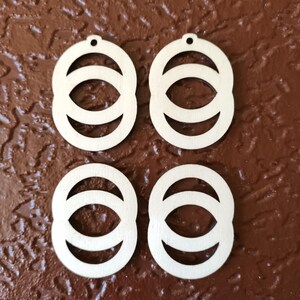 May include: Four unfinished wooden earrings with a circle design. Each earring has three concentric circles, with the inner circle being the smallest and the outer circle being the largest.
