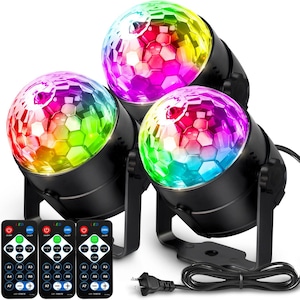 May include: Three black disco ball lights with multi-coloured, faceted globes. Each light has a stand and a remote control. The globes display a spectrum of colours, including red, green, blue, and yellow. A power cord and plug are also visible.