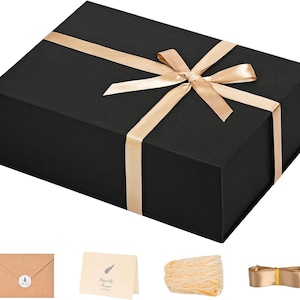 May include: A black gift box with a gold satin ribbon tied in a bow. The box is rectangular and has a matte finish. Additional items include a kraft paper envelope, a card, shredded paper, and a ribbon.