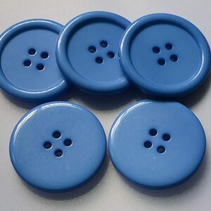 May include: Five round, light blue buttons with four holes each. The buttons have a glossy finish and a raised outer rim. These sewing notions are suitable for various craft and apparel projects.