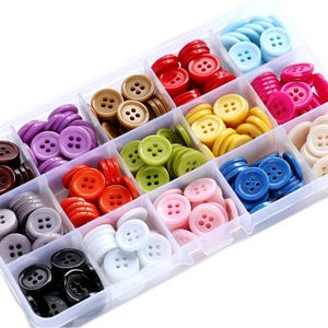 May include: A clear plastic organiser containing a variety of colourful buttons. The buttons are in shades of red, blue, yellow, pink, green, and brown. Each button is round with four holes. The organiser is divided into compartments.